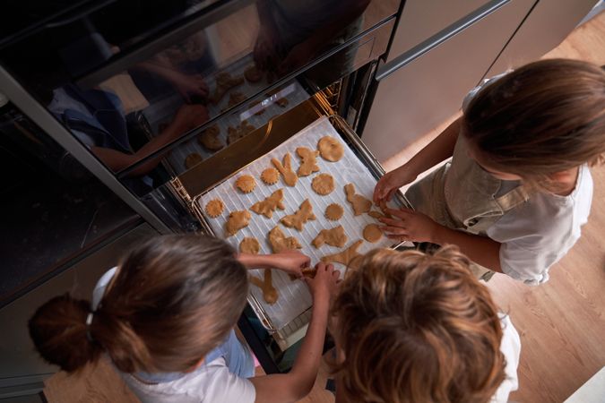 Unrecognizable children arranging cookies on oven rack