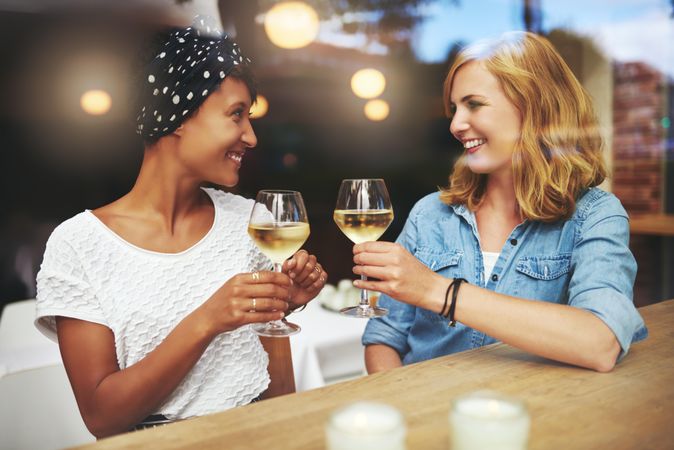 Two female friends sitting at a cafe table toasting with wine