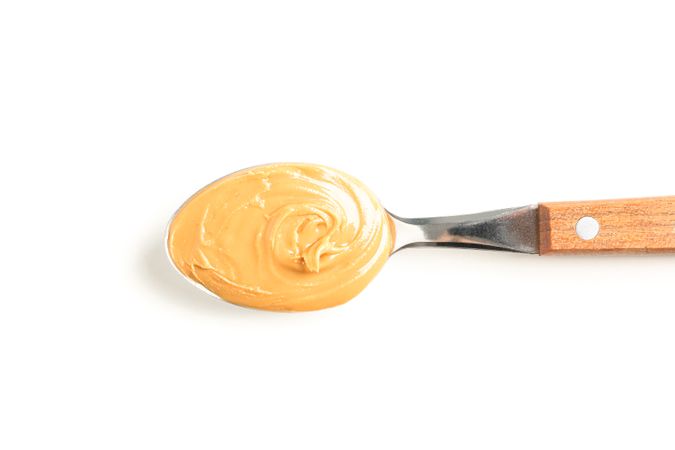 Creamy peanut butter in spoon isolated on light background, top view. A traditional product of American cuisine