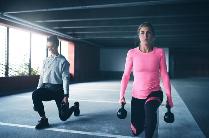 Two women doing lunges with kettle bells