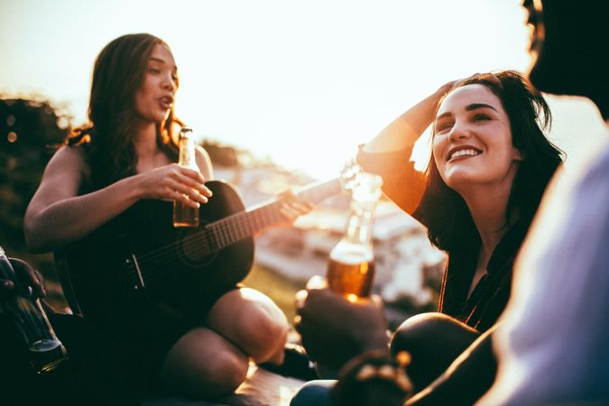 A group of friends enjoy the sunset with beer and a guitar