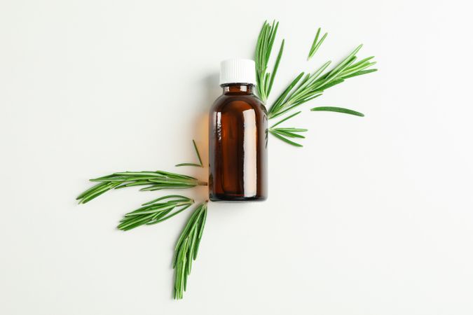 Flat lay composition with rosemary oil and leaves on plain background, space for text