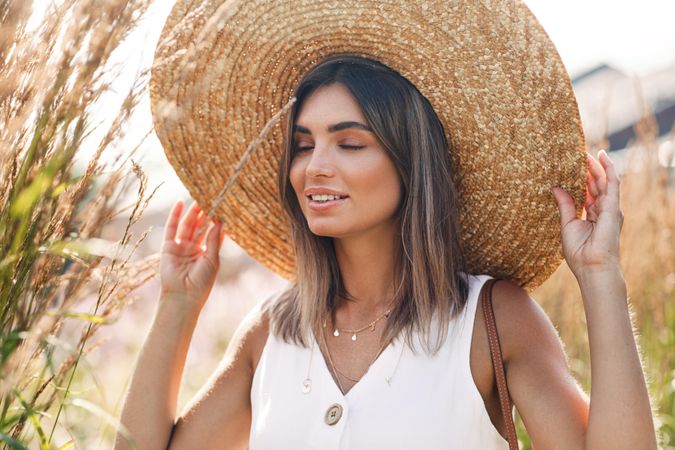 Content woman in field wearing a large straw hat with her eyes closed