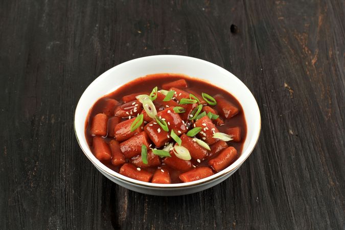 Bowl of Korean rice cakes in spicy sauce served on wooden table