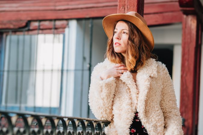 Smiling woman in warm wear standing near building and fence