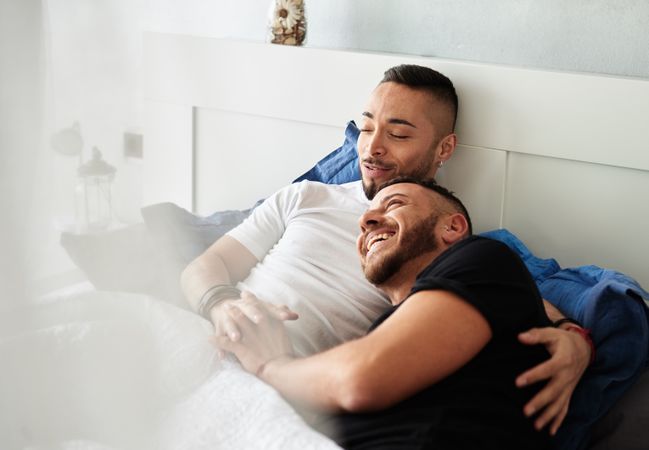 Smiling gay couple hugging on bed