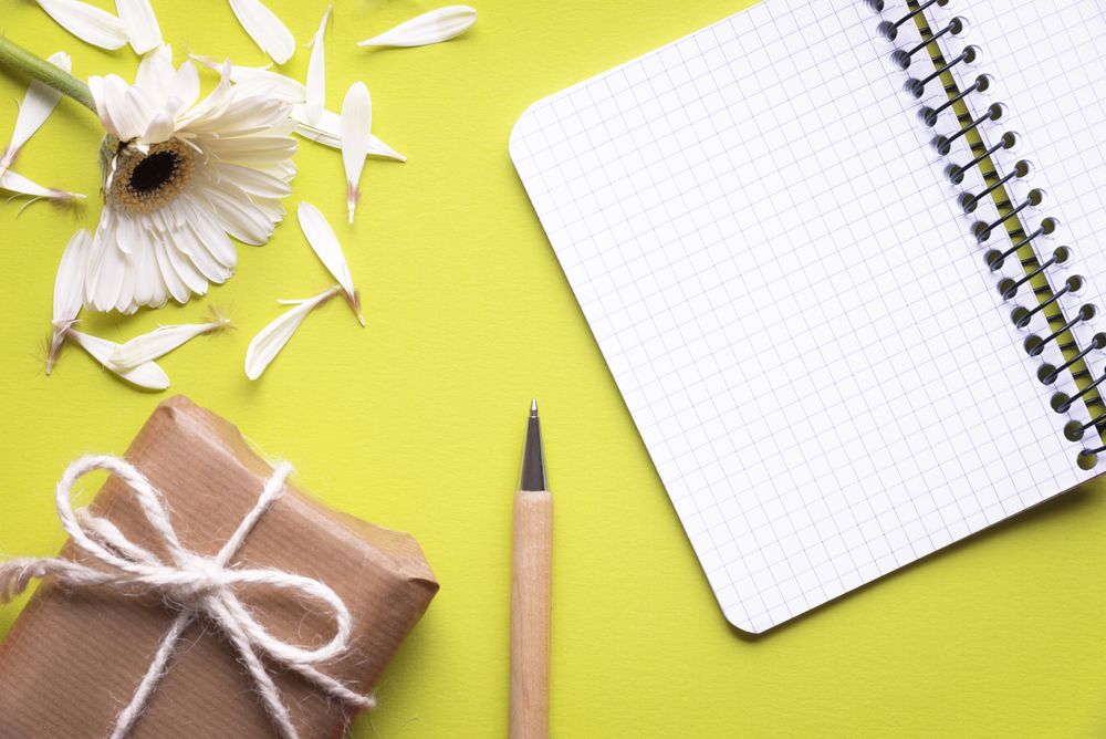 Flat lay of blank notebook with flower and gift in brown paper