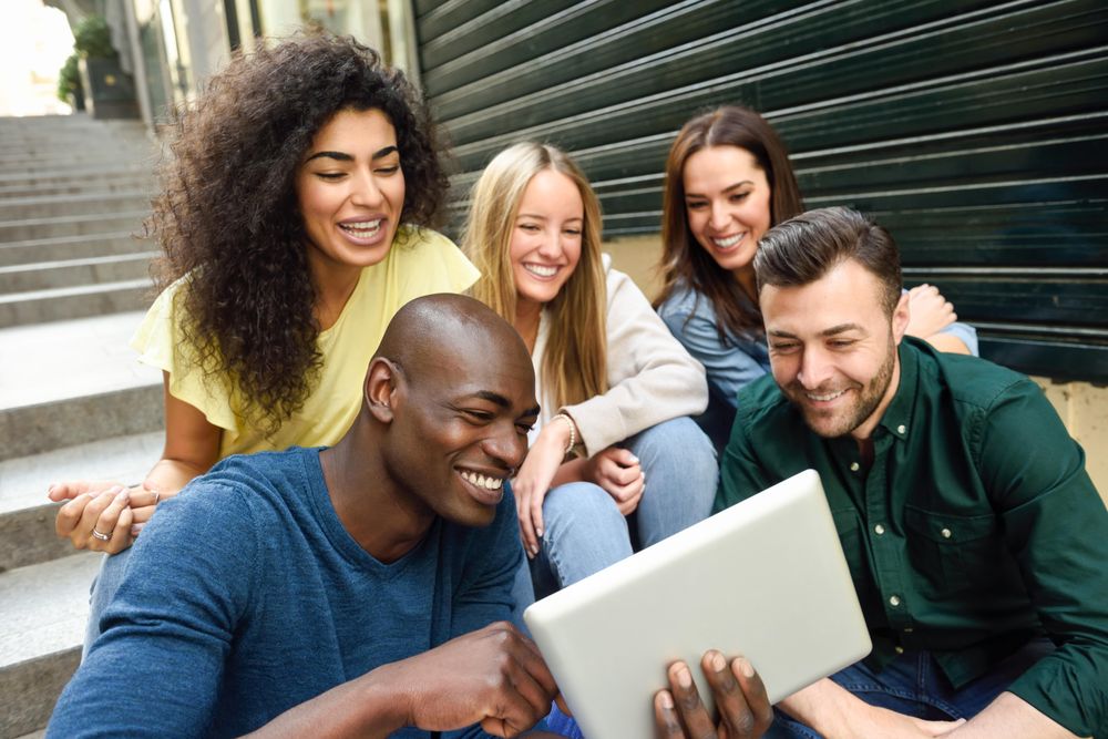Friends engaged by something on digital tablet while sitting on outdoor cement staircase