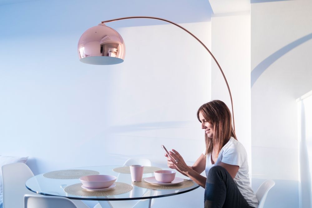 Woman sitting at breakfast table texting on phone in front of cereal bowl