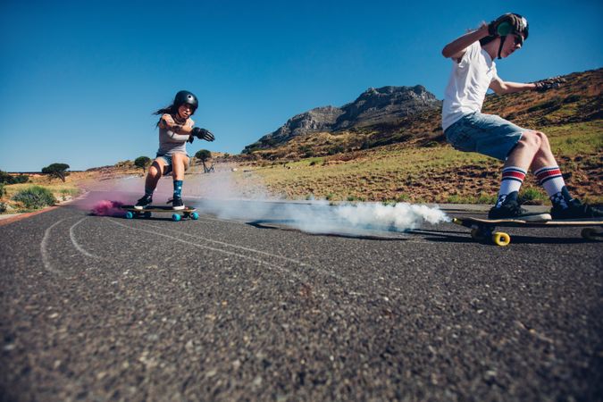 Young man and woman practicing skating on skateboard with smoke grenade