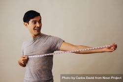 Smiling Hispanic male holding out measuring tape in beige studio shoot bexwP4