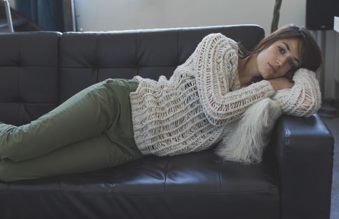 Female in wooly sweater lying on her side trying to nap on leather couch in living room
