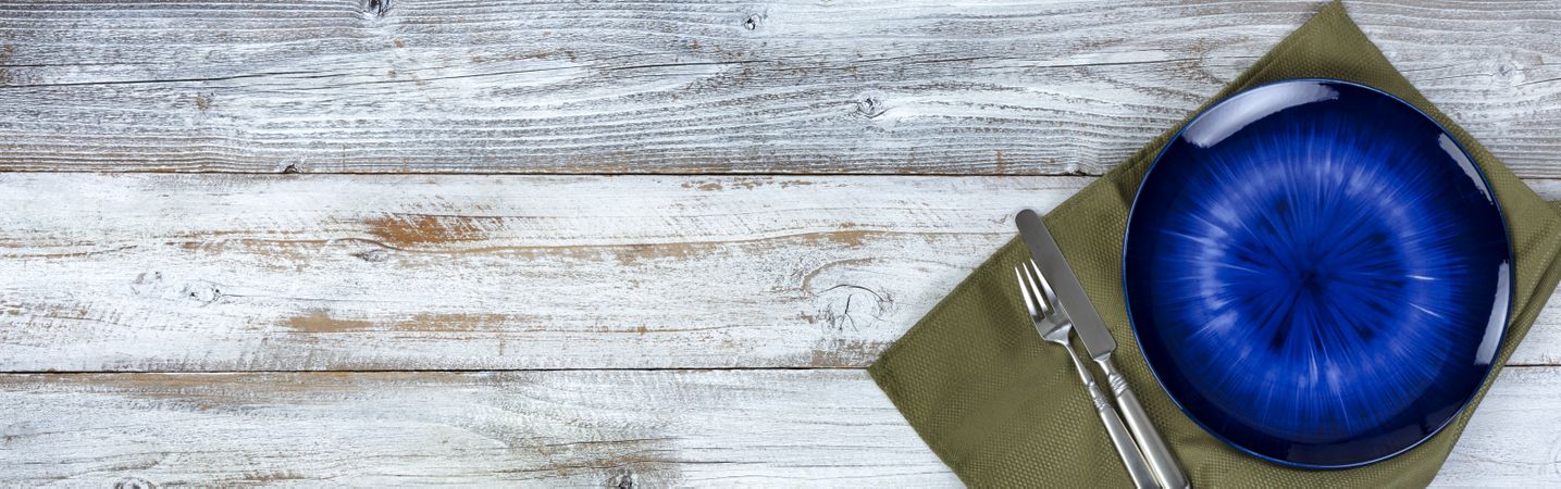 Basic table setting of an empty main dark blue dish with green cloth napkin and cutlery