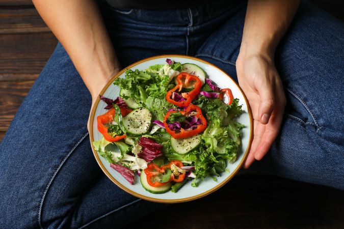 Young woman in jeans holding salad on wooden background