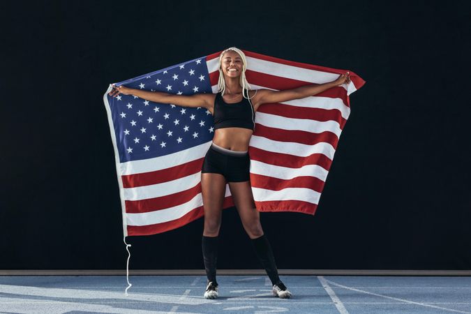 Smiling female sprinter standing on running track holding the US flag