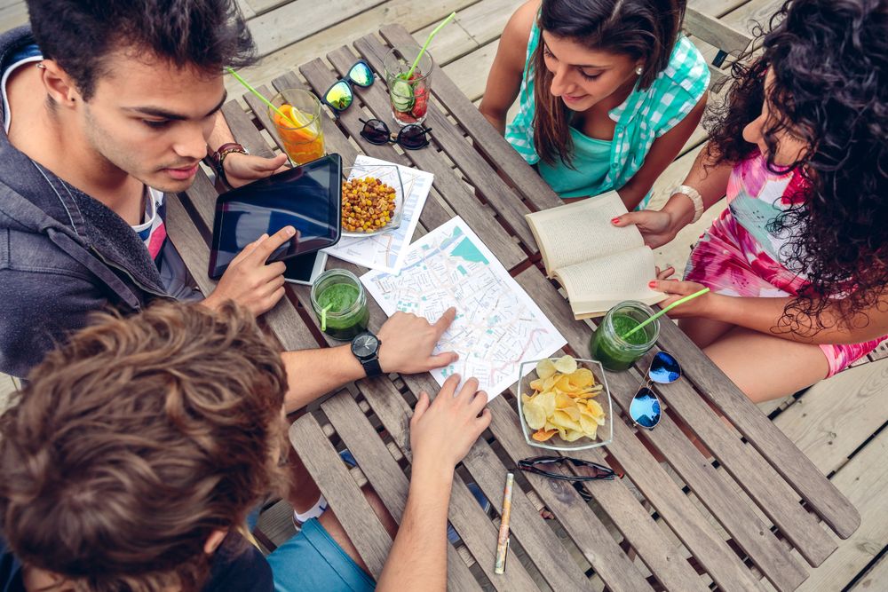 Friends sitting on bench with snacks reviewing maps