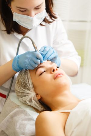Woman having beauty treatment with instrument on her forehead, vertical