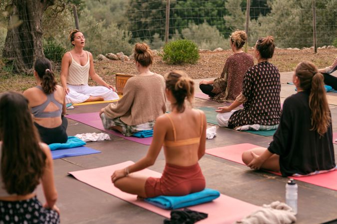 Group of women practicing Lotus pose with instructor outdoors