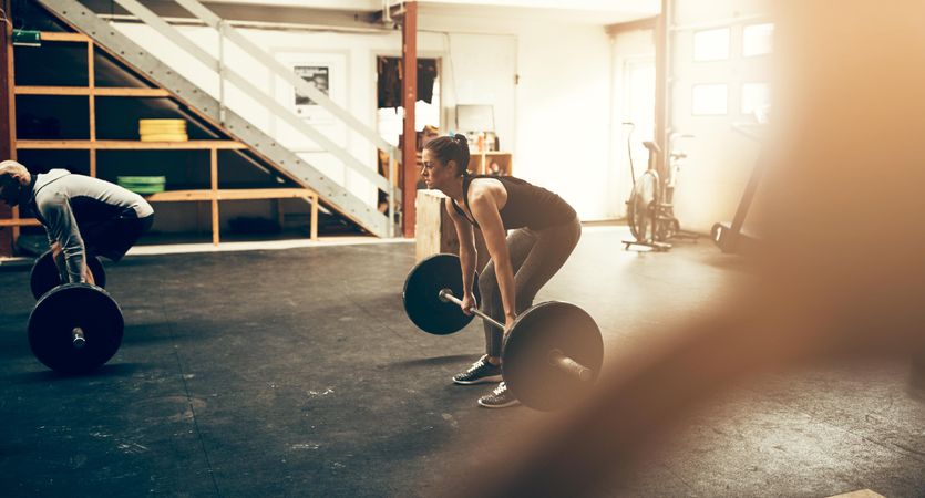 Side view of woman performing deadlifts in busy gym