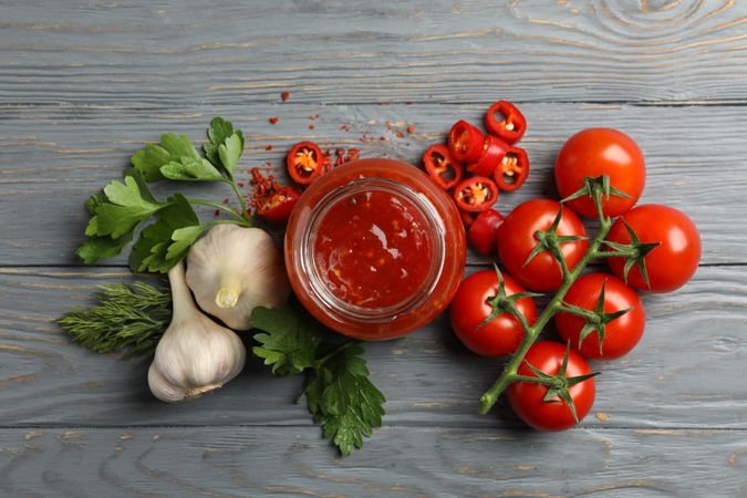 Jar with red chilli and tomato sauce, and spices on wooden table