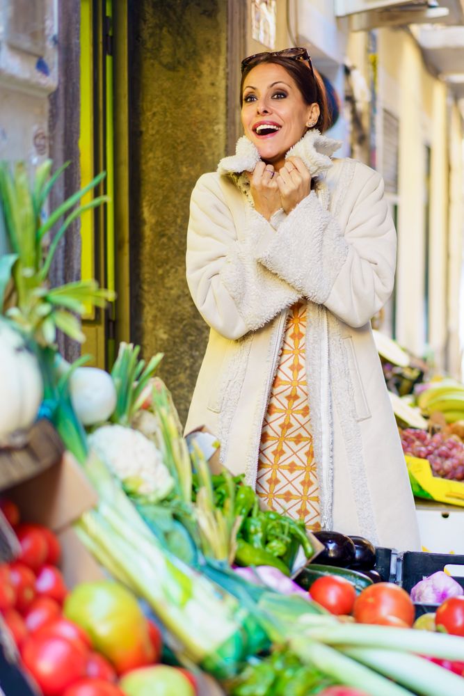 Smiling woman standing by colorful ripe fruits and vegetables in shop