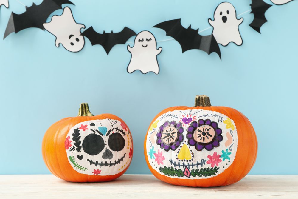 Pumpkins with catrina skull makeup, ghosts and bats on blue background