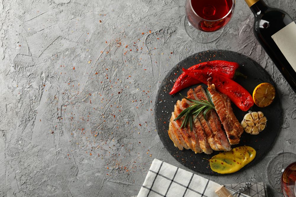 Chopped fried pork steak, vegetables and wine on gray background. Grilled food