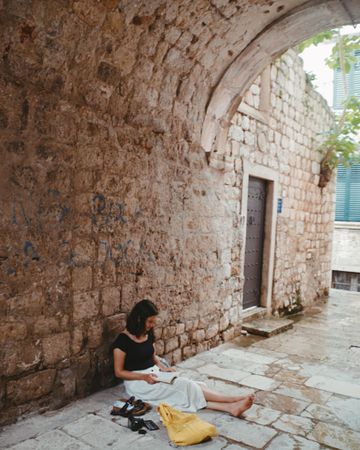 Woman sitting on grey ground beside an old house outdoor