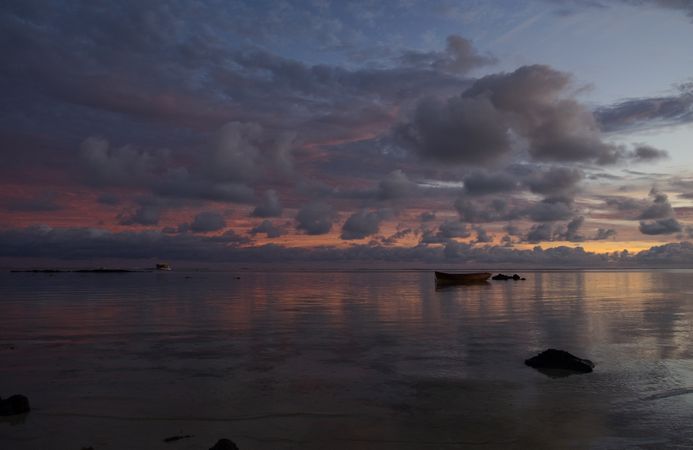 A single boat on a vast ocean at dawn under a cloudy sky