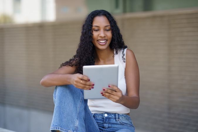 A Young Woman Engaged with a Tablet in a Bustling Urban Setting During Daylight Hours