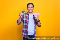 Happy Asian man holding credit card and cash in studio shoot 486YJ0