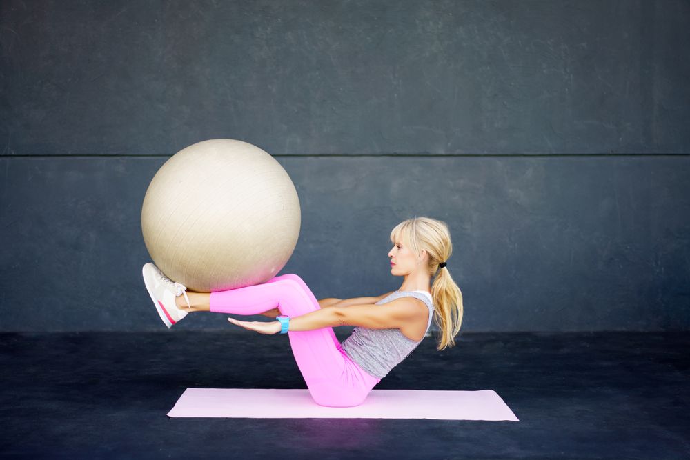 Slim woman doing yoga with fitness ball in studio