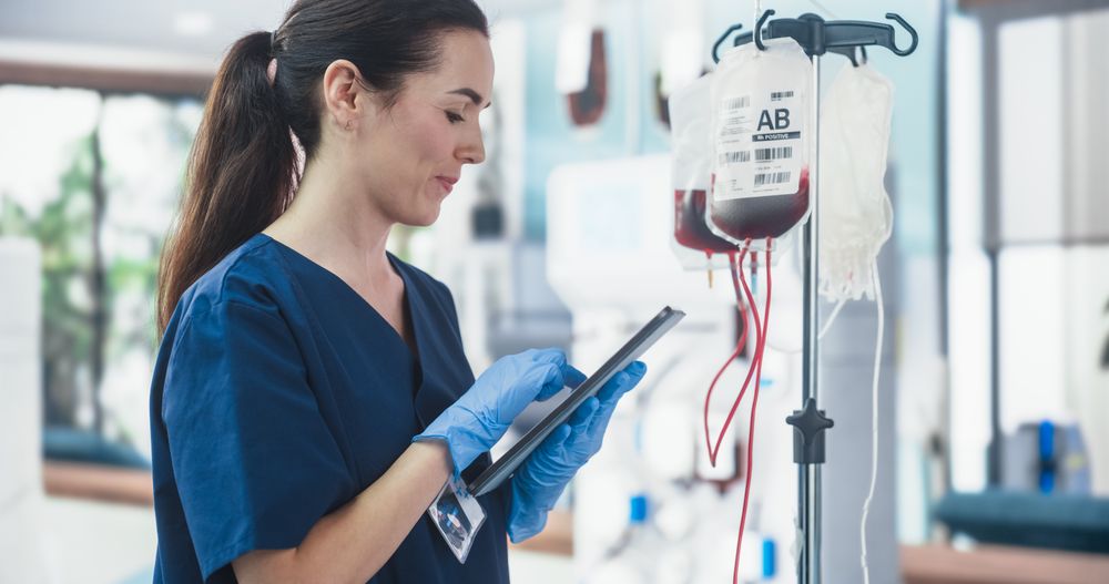 Female Nurse Holding Tablet Computer And Checking The Blood Bag In Donation Center.