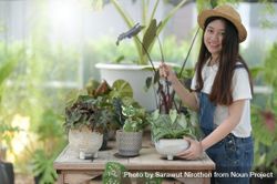 Smiling Asian female in a green house working with plants on a table 0WgMW0