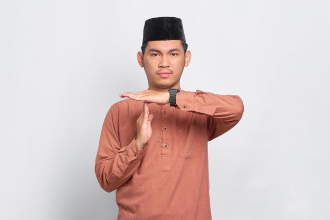Muslim man in kufi cap making “time out” gesture with hands