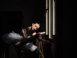 Young ballerina stretching leg on barre in dark room