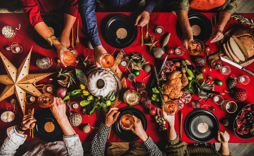 Group of people with drinks at festive red table setting with cake, roast chicken, decorations