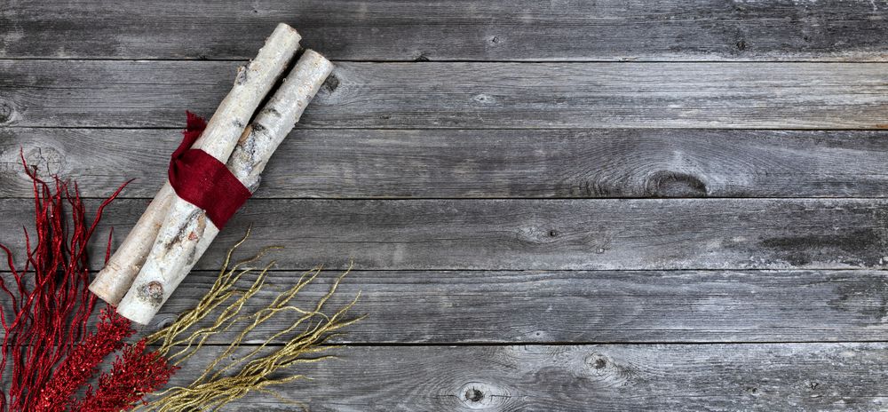 Top view of decorated birch logs wrapped in cloth with red and golden flaming decorations on age wooden planks for a Merry Christmas background