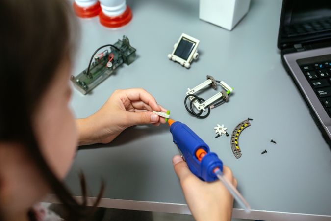 Student using hot melt glue gun on machine pieces in robotics class