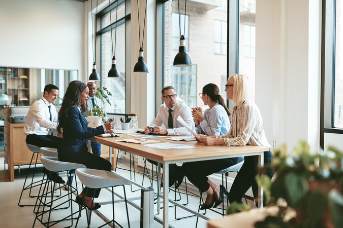 Group of people discussing work at a long table in a bright office