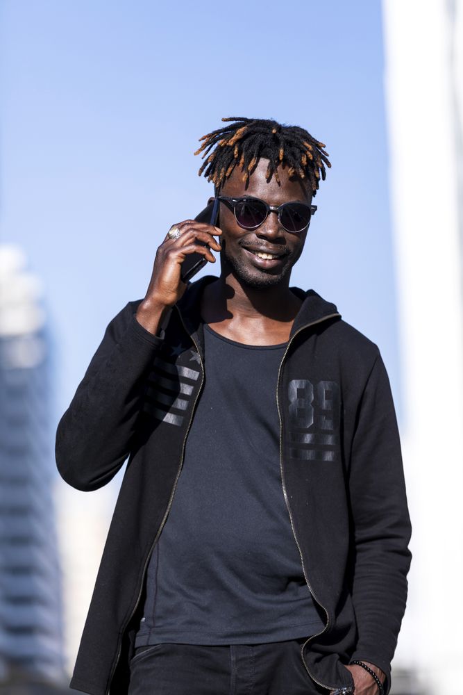 Front view of Black man with sunglasses standing against cityscape on the street while using a mobile phone in sunny day