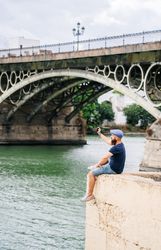 Guy on vacation in casual clothing making photo of bay on smartphone at quay