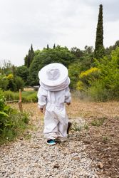 Child in protective costume standing near bee smoker