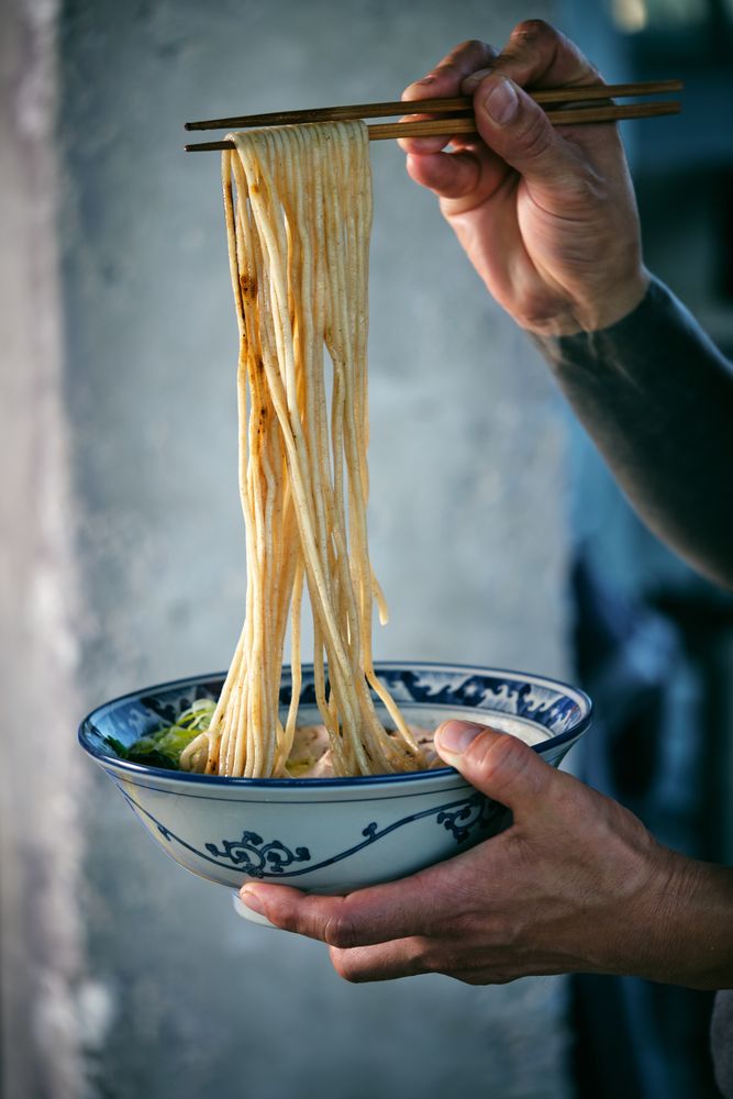 Crop man with noodles on chopsticks above tasty ramen