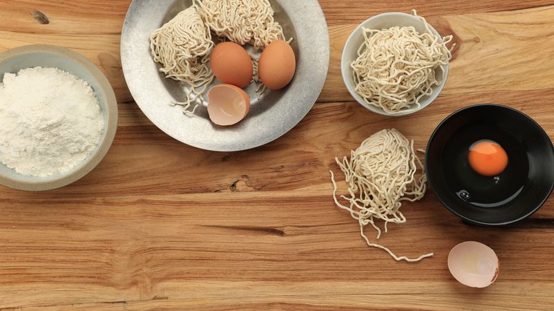 Top view of eggs, flour and noodles on wooden table