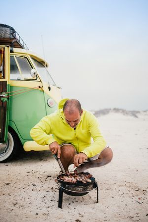 Tanned man cooking on camping stove beside parked mini van