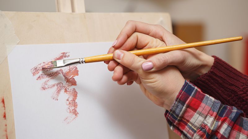 A teachers hand guides an art students paintbrush