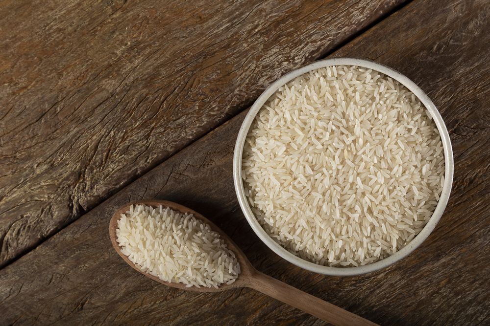 Rice in a ceramic bowl on brown wooden background.