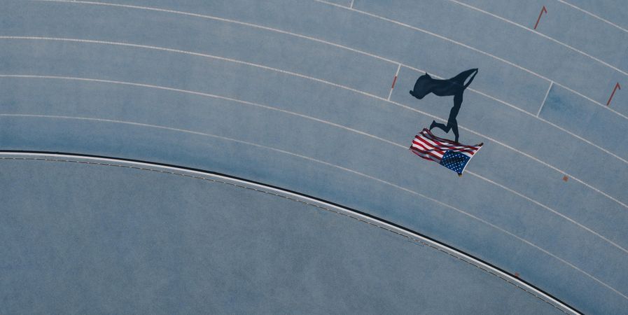 Aerial view of an athlete running on athletic track holding the American flag over the head