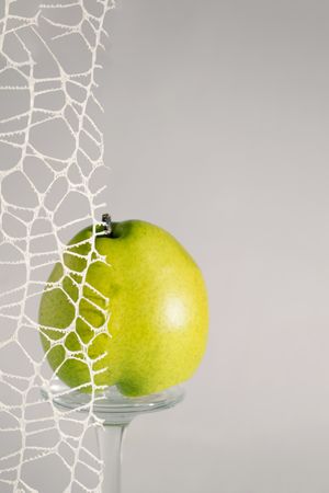 Green pear balancing on glass behind lace